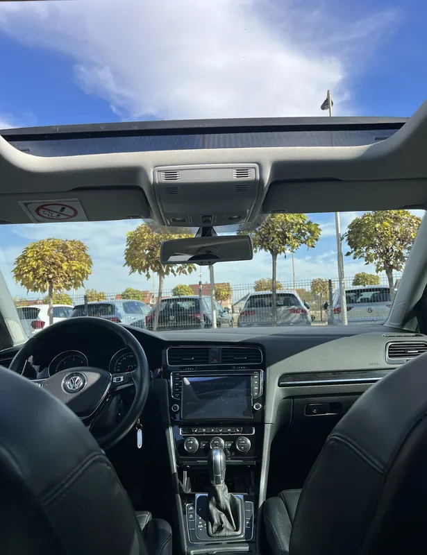 Inside a Volkswagen: steering wheel, touchscreen, automatic gear lever and an open glass roof